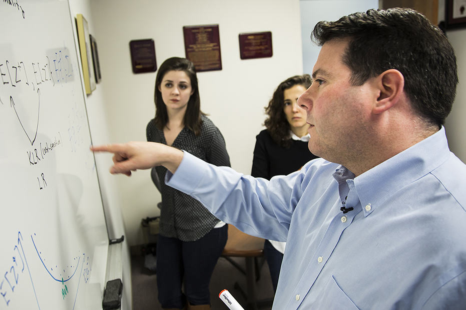 Researcher Brian Denton stands at whiteboard instructing his graduate students