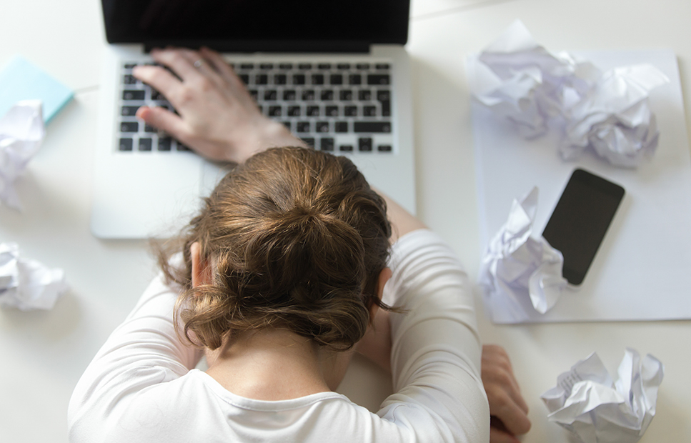 Person with head down. Crumpled papers and laptop surrounding.