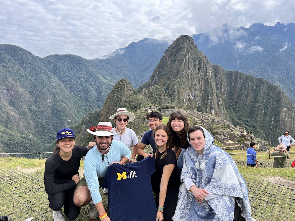 Alexios and peers holding up an IOE t-shirt in front of a mountain