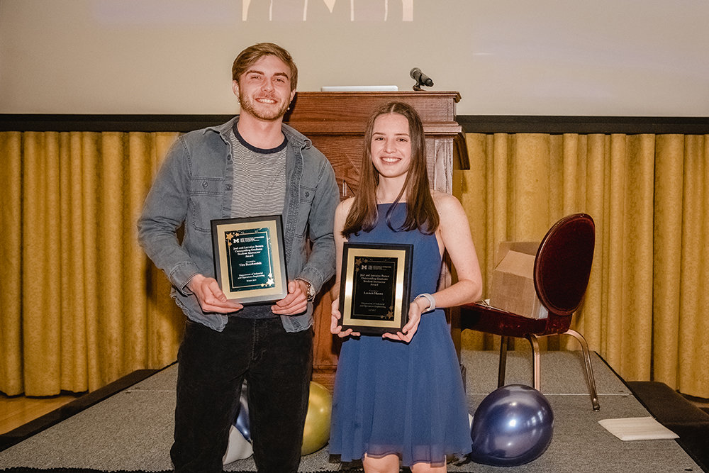 Two people stand smiling holding a award plaque 