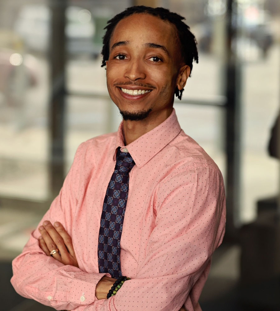 Alonzo Wilson portrait. Wearing a pink dotted shirt with a purple tie crossing his arms.