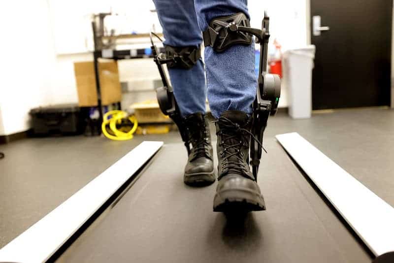 Person walking on treadmill attached to exoskeletons